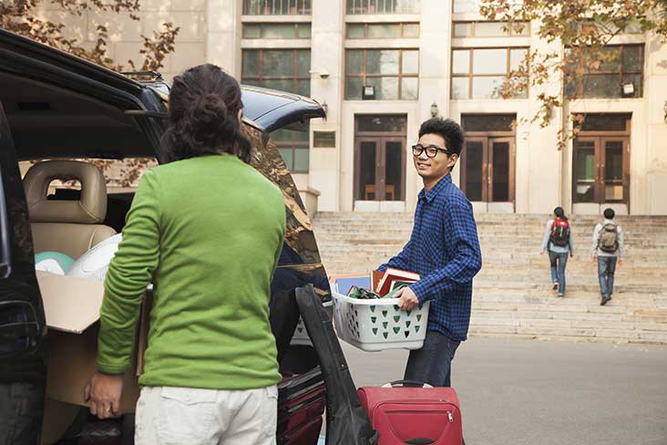 a college student and his mom unpacking a car in front of a dorm